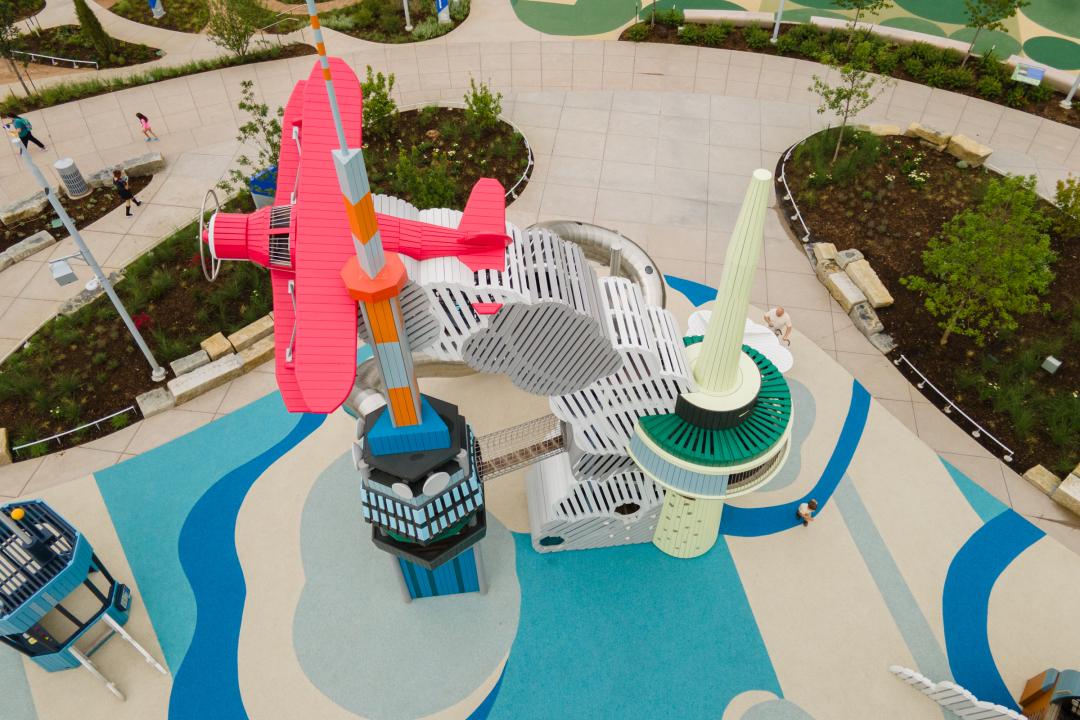 Playground with wooden staggerwing plane flying above control towers and with billowing exhaust fumes below