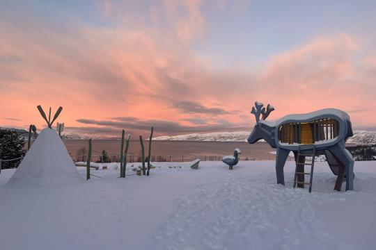 A playground in snow with deer and tent structures on waterfront