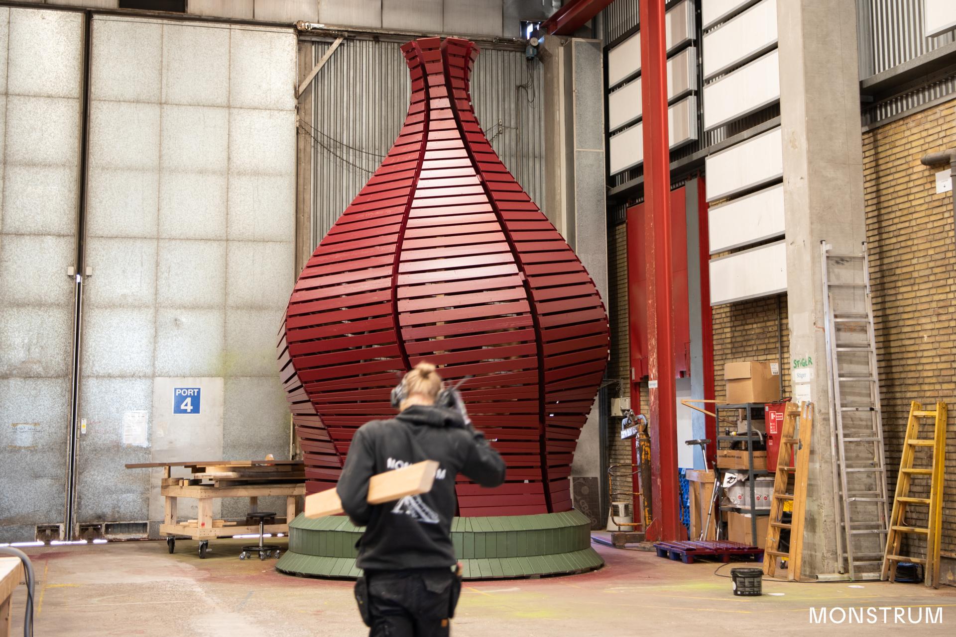 Carpenter walking through the MONSTRUM workshop in front of a giant elf's hat for tower