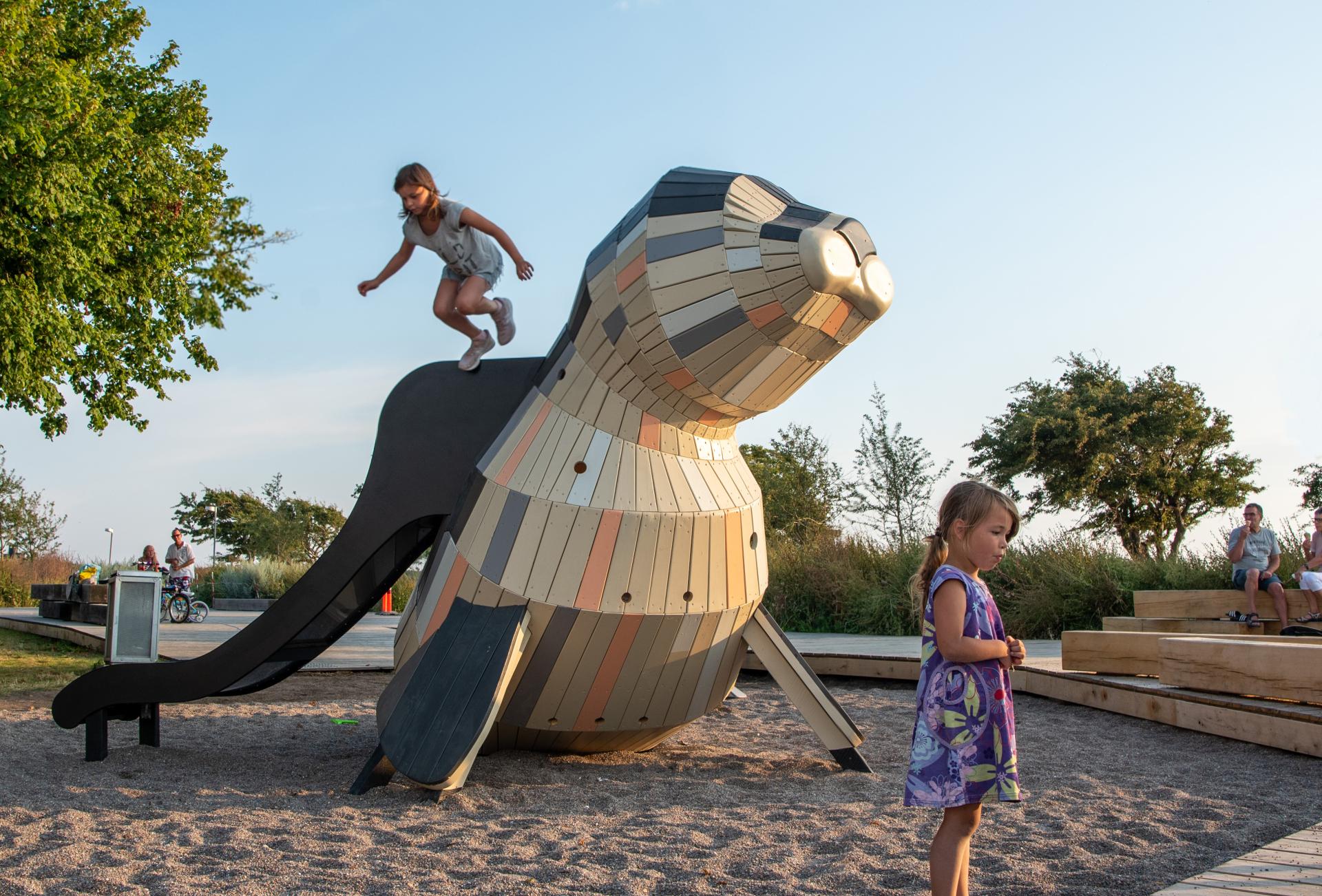 Girl jumping from slide on seal play structure at MONSTRUM playground
