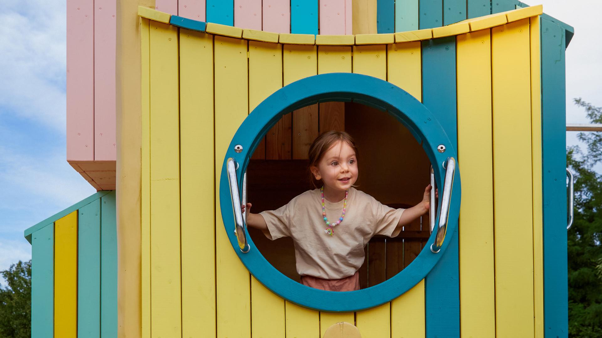 Girl peeking out from giant birdhouse at playground