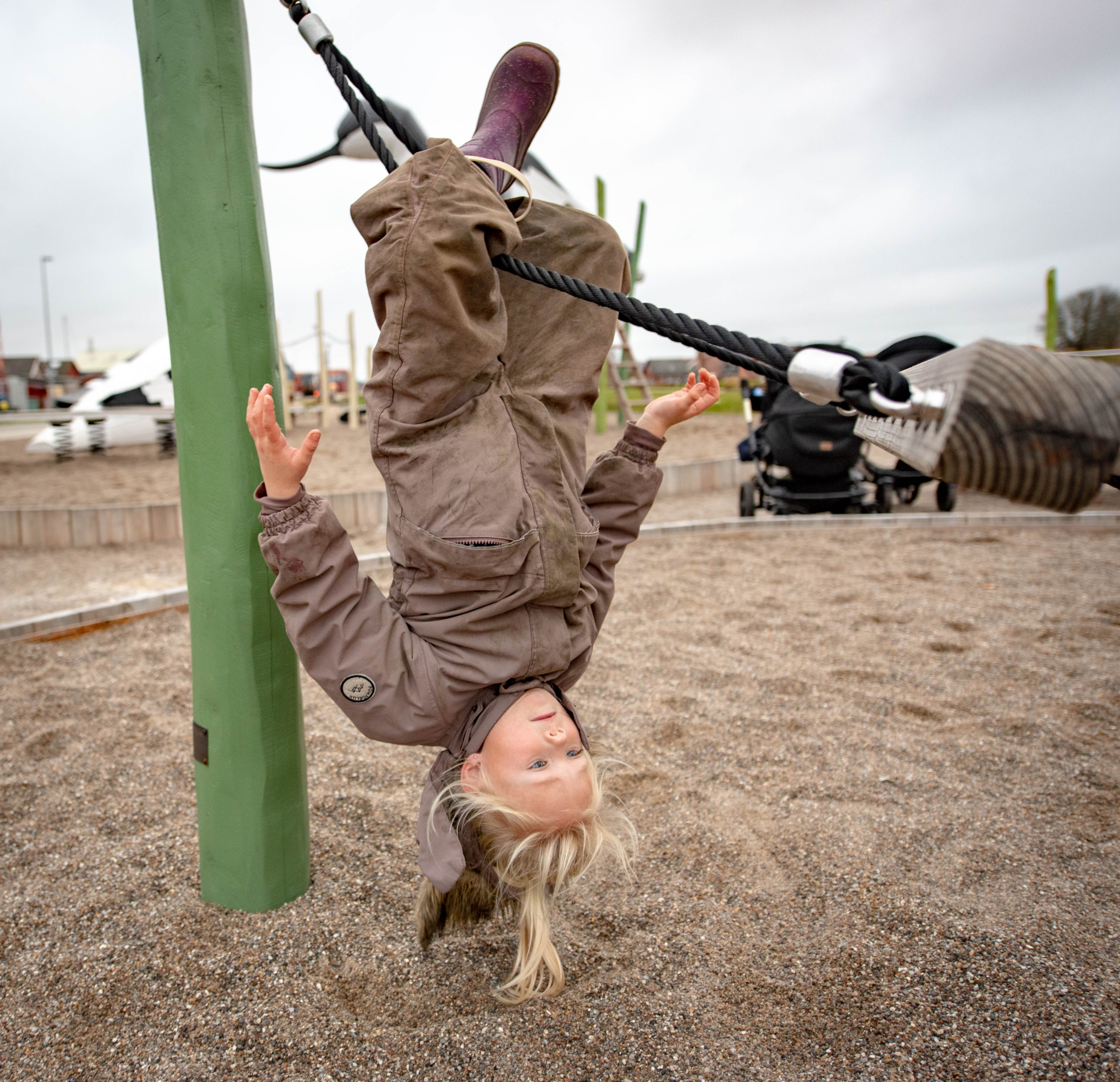 Girl hanging upside down on hammock play feature at playground