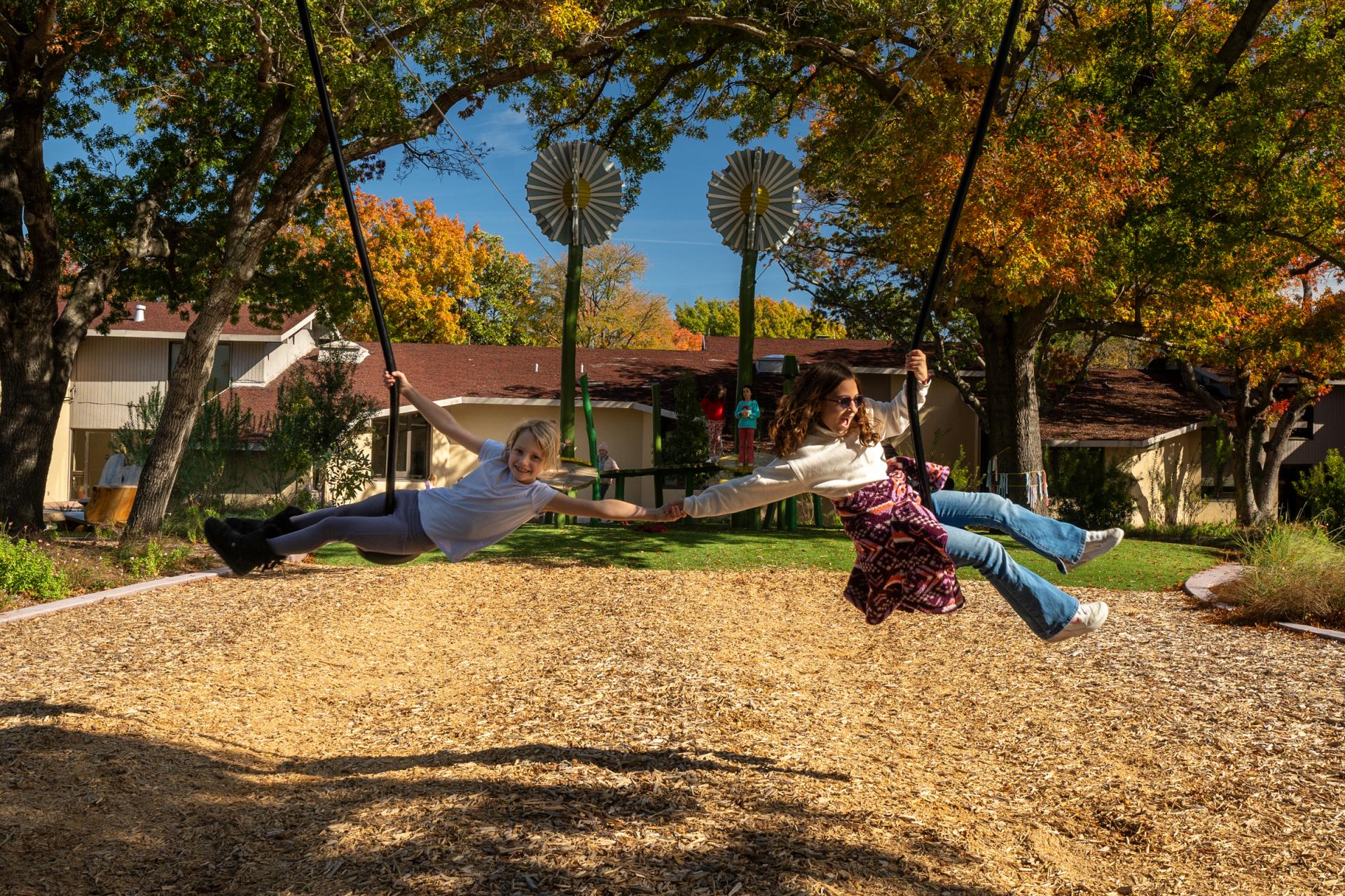 Two girls holding hangs on zip slide at school playground 