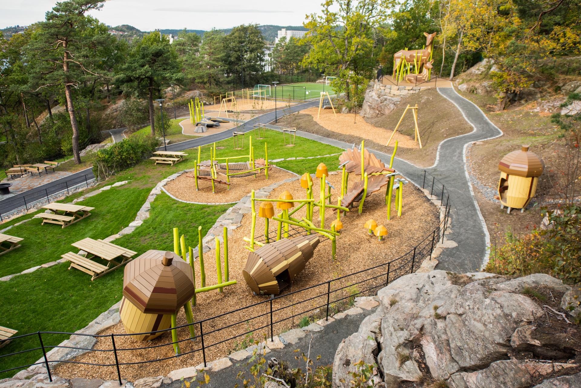 Artistic wooden playground featuring two deer and other plant and animal life spread across several levels in park area