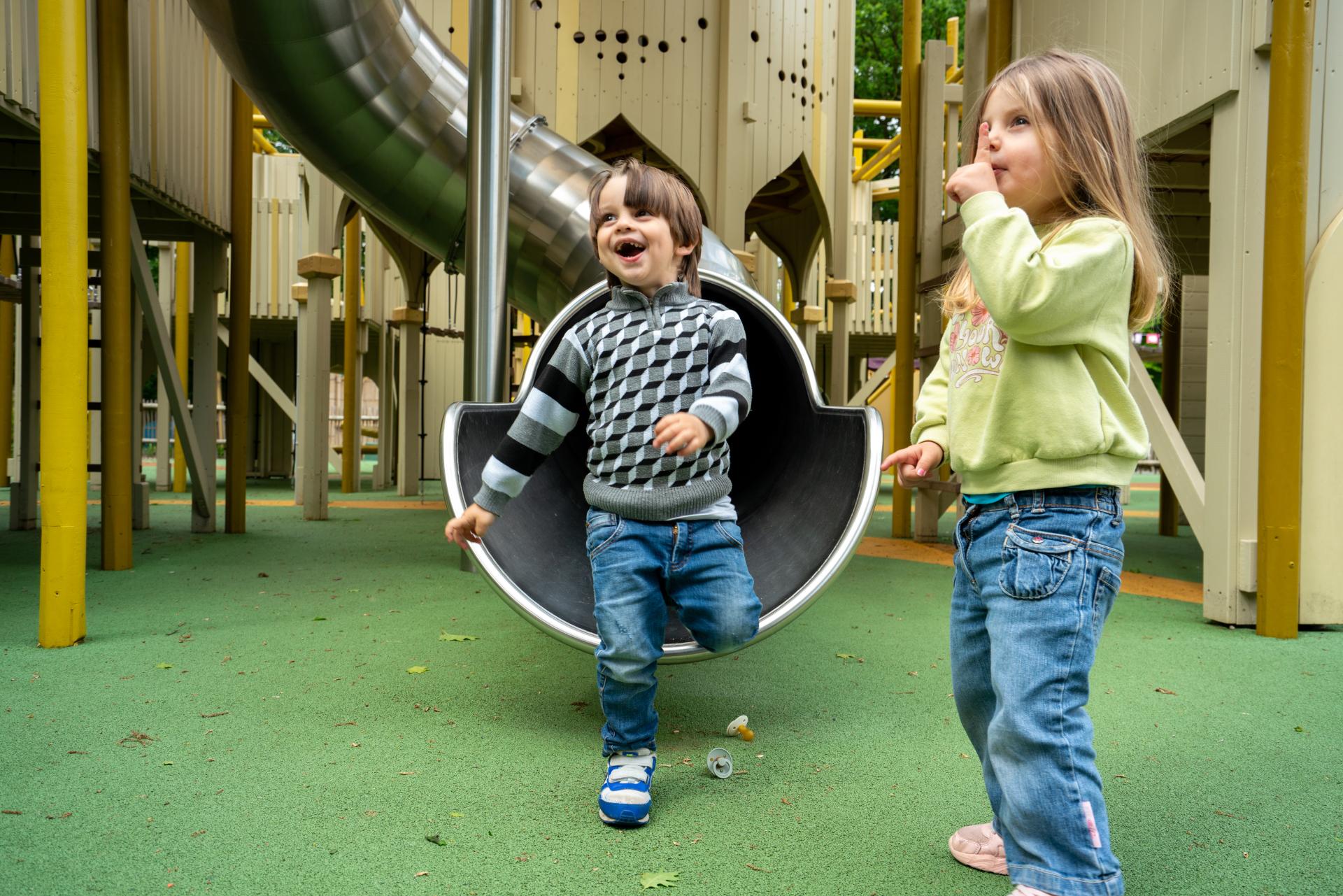 Girl and boy smiling after sliding down playground slide