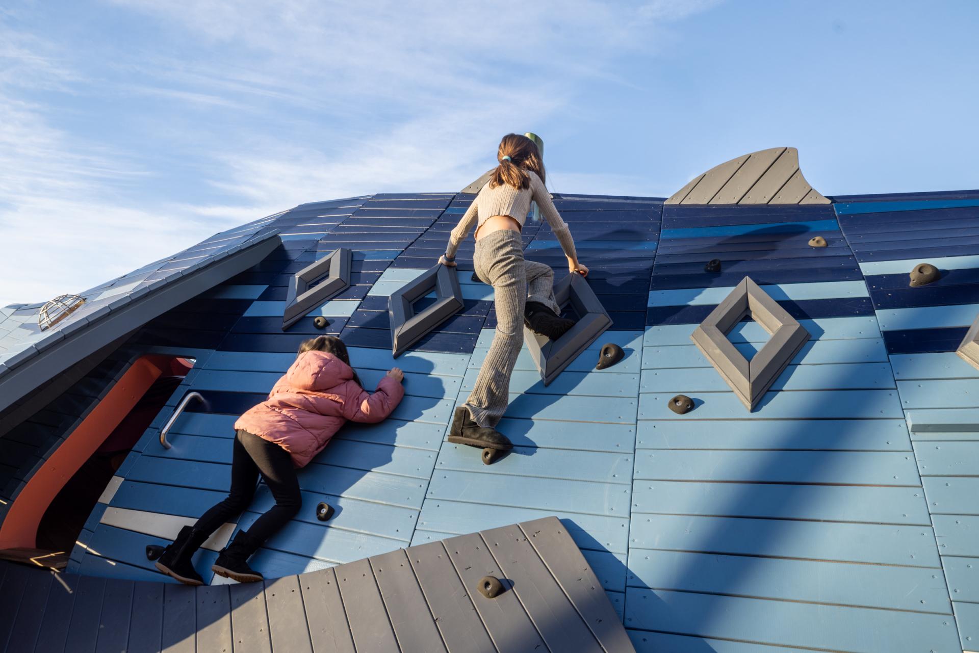 Girls climbing up on huge fish playground climber