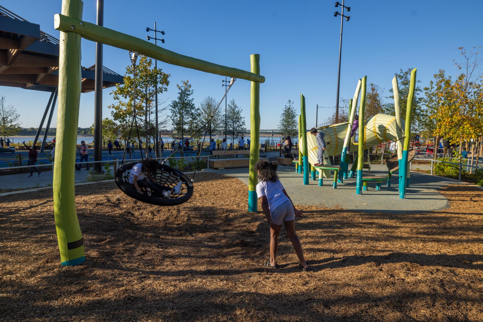 Kids playing on basket swing at riverfront playground at Tom Lee Park