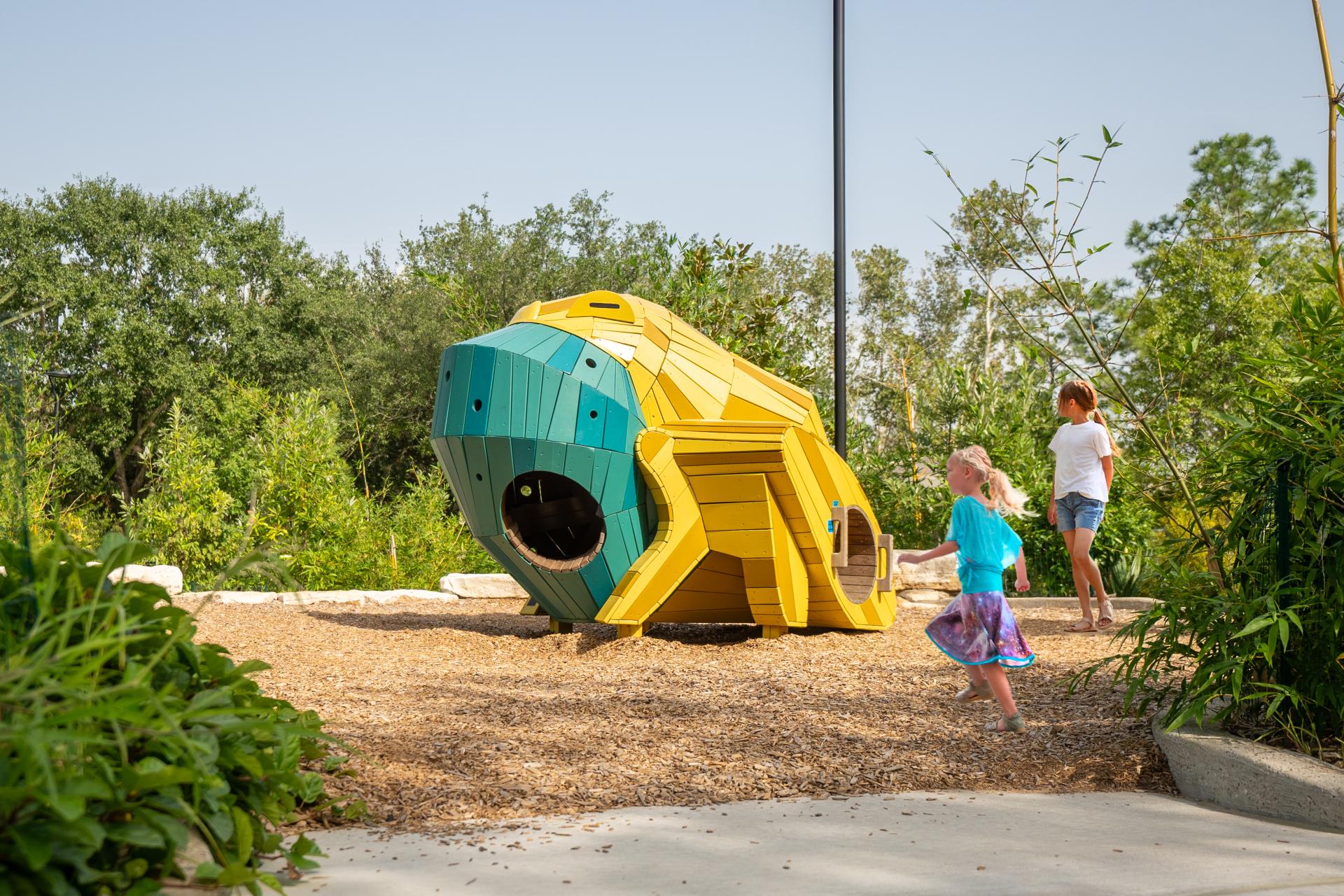 Girls playing and running by frog playground structure