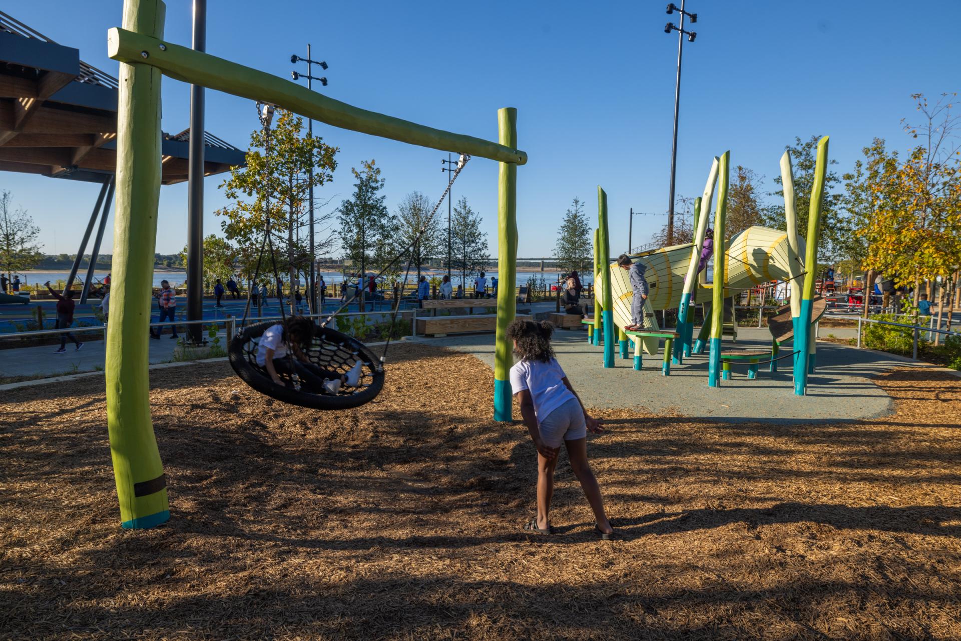 Kids playing on basket swing at riverfront playground at Tom Lee Park