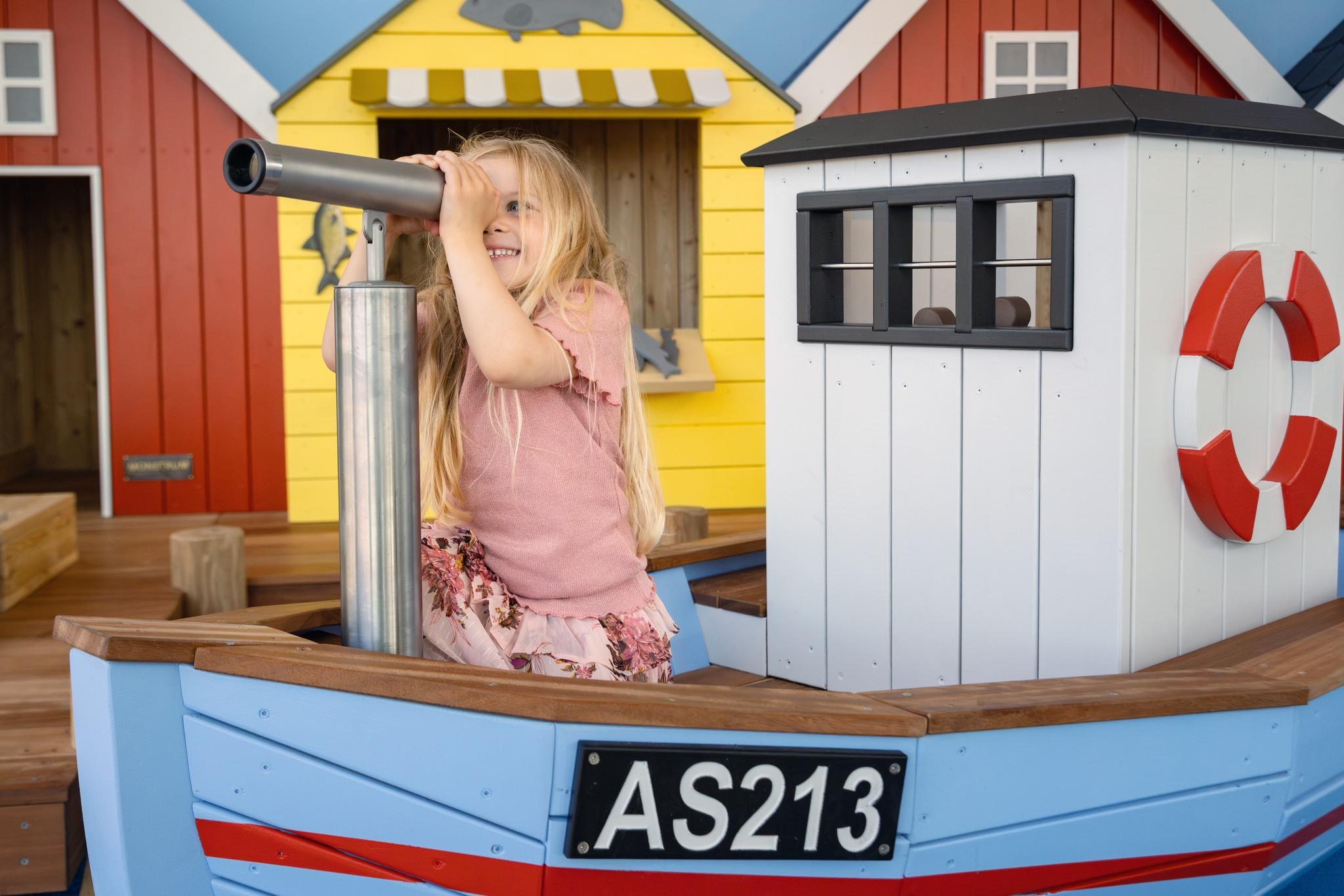 Girl looking through spyglass at maritime themed playground