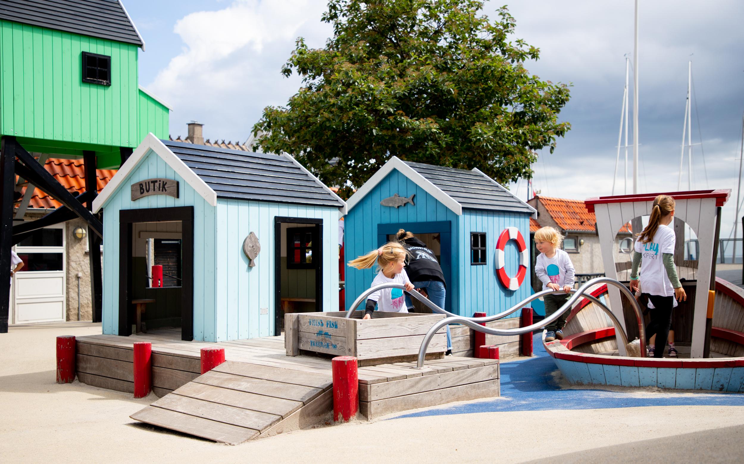 Children playing with wooden fish they're sliding along metal poles at creative playground