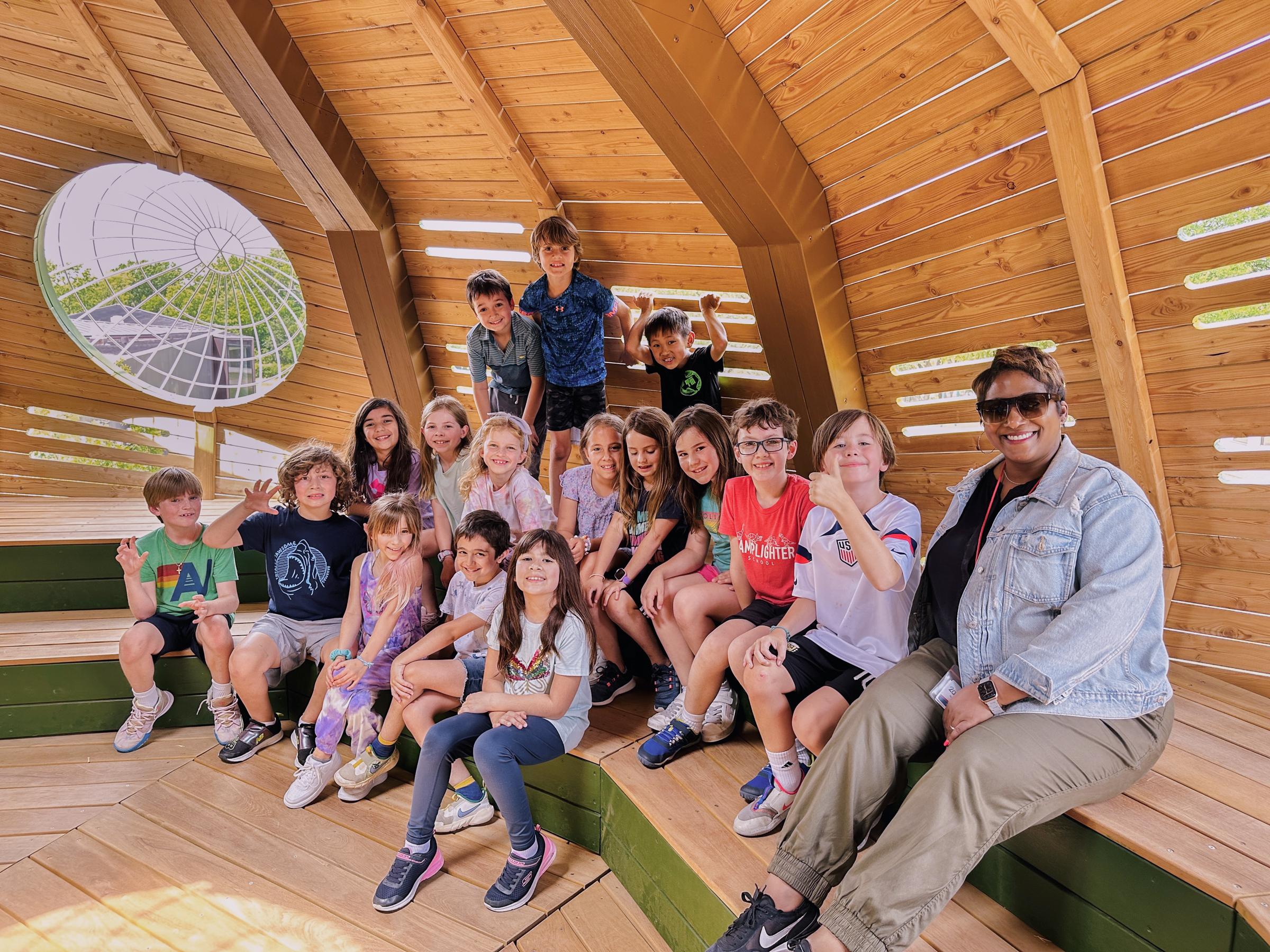 Group of students and their teacher sitting in huge wooden tree structure