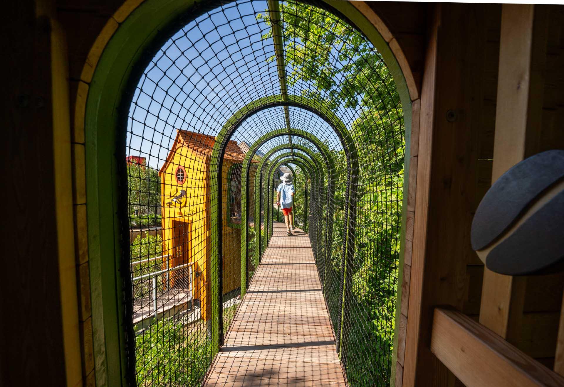 Boy running through suspended playground tunnel