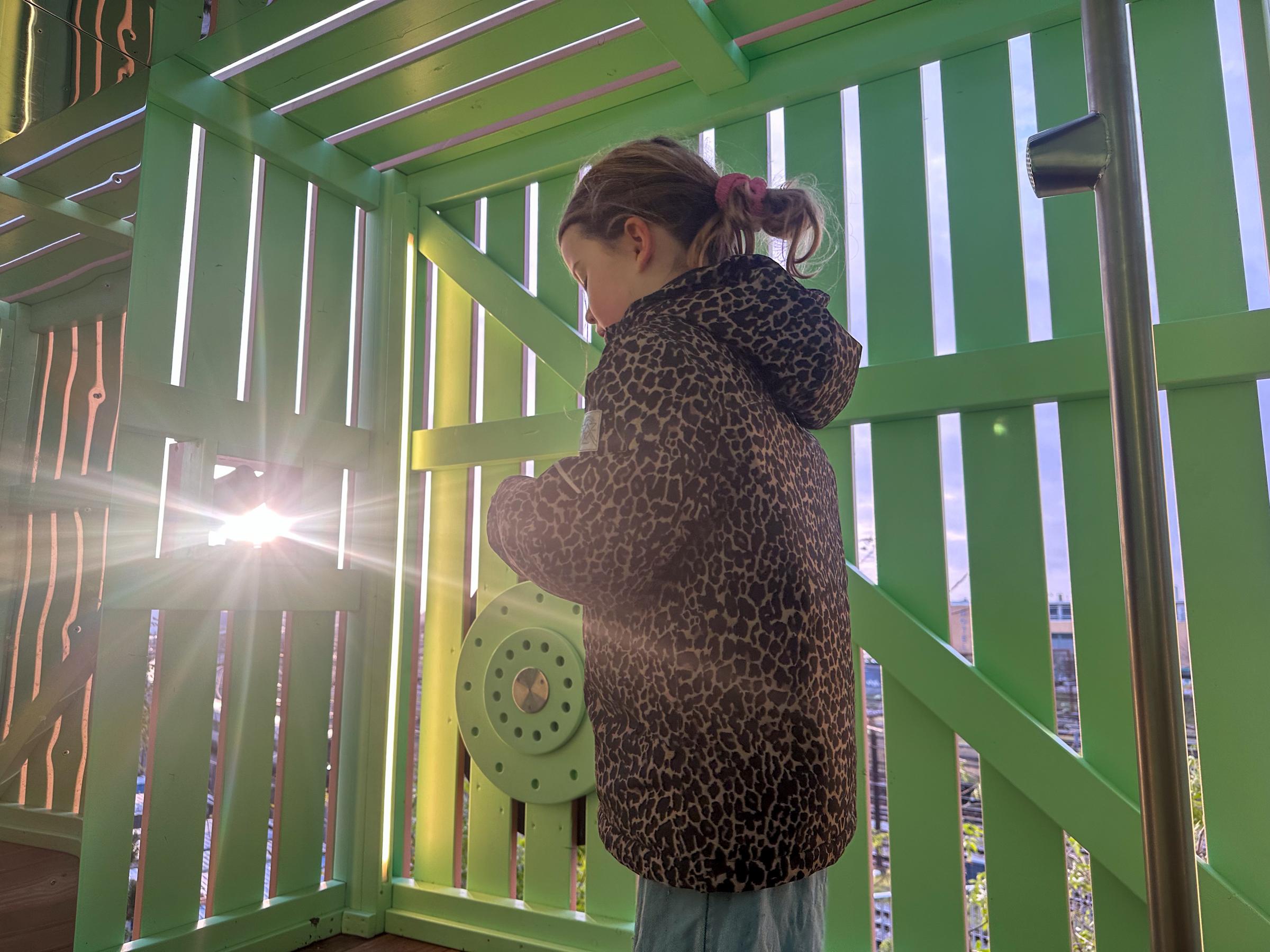 Girl inside playground tower with light streaming in between wooden boards