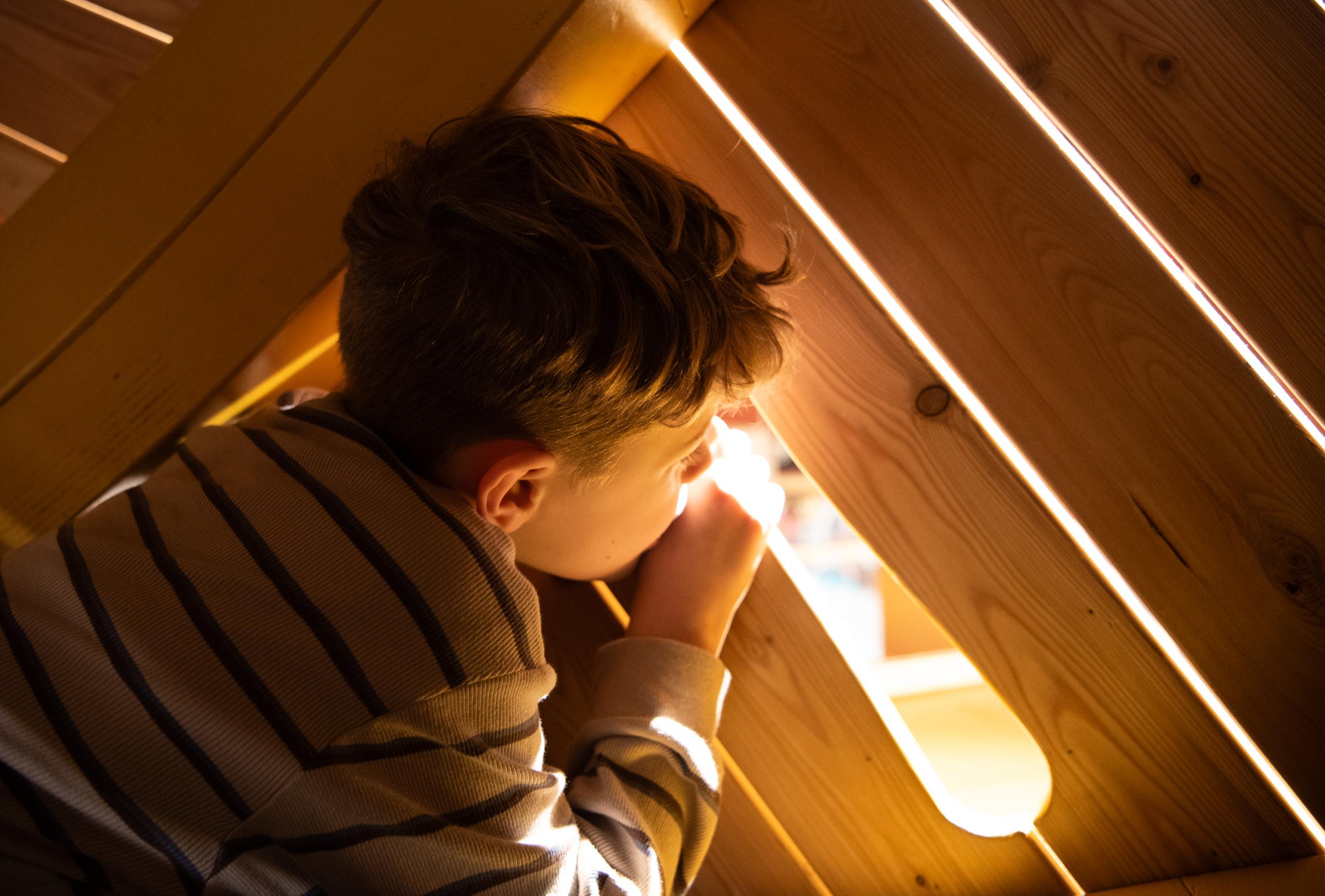 Boy looking out through opening in wooden playground