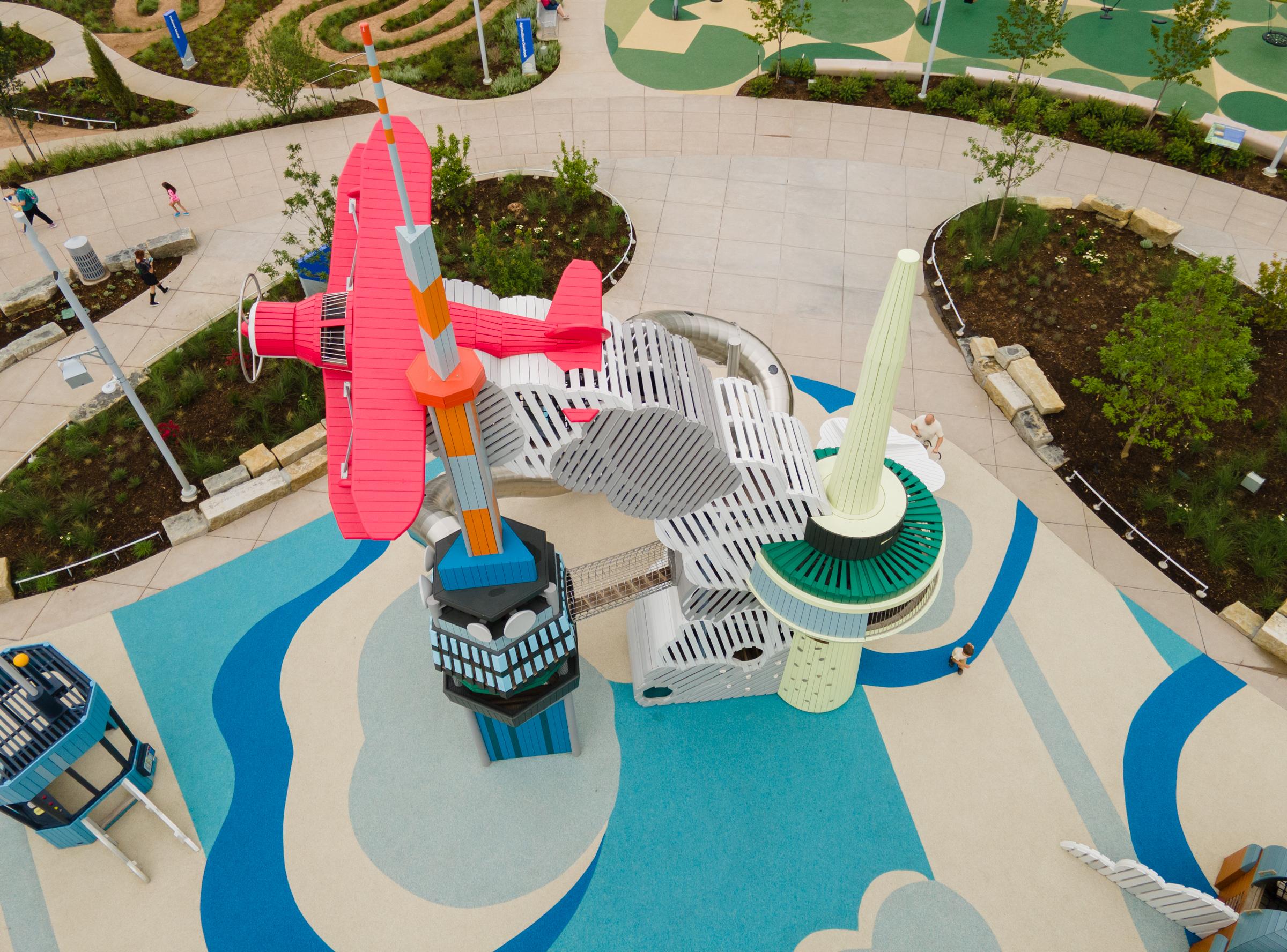 Playground with wooden staggerwing plane flying above control towers and with billowing exhaust fumes below