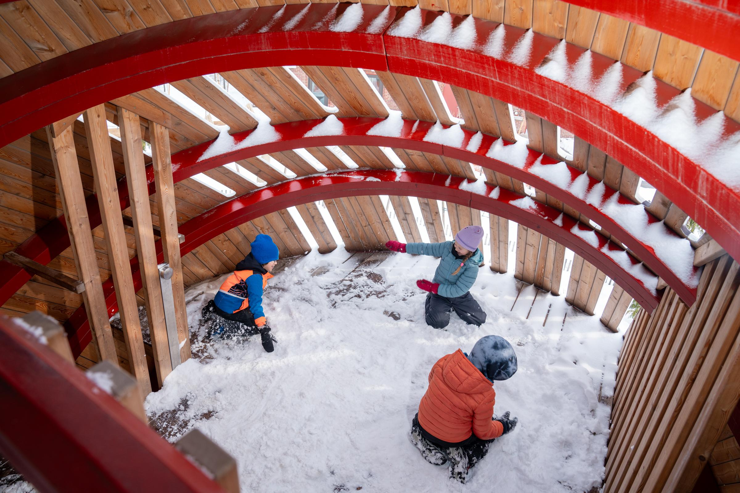 Kids playing in the snow inside big wooden owl playground
