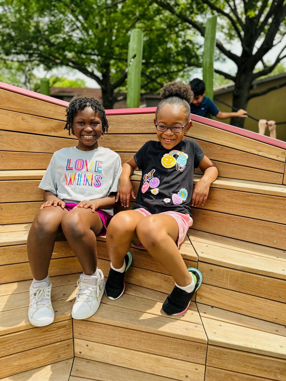 Two kids sitting smiling on wooden worm play structure