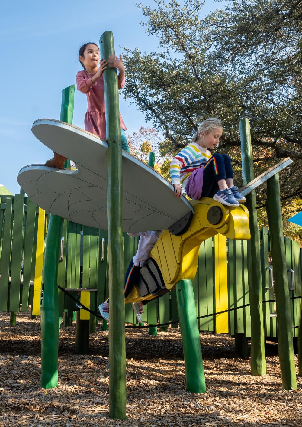 Girls climbing on giant wooden firefly at playground