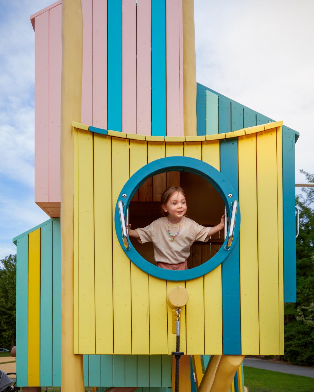 Girl looking out from huge birdhouse playhouse at playground