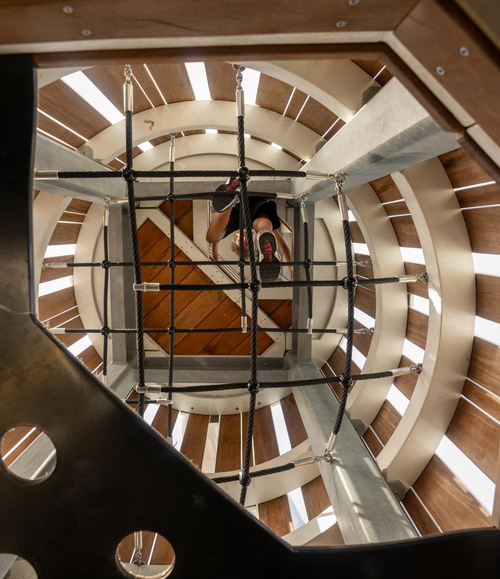 Boy seen from below climbing up climbing nets in rocket playground tower