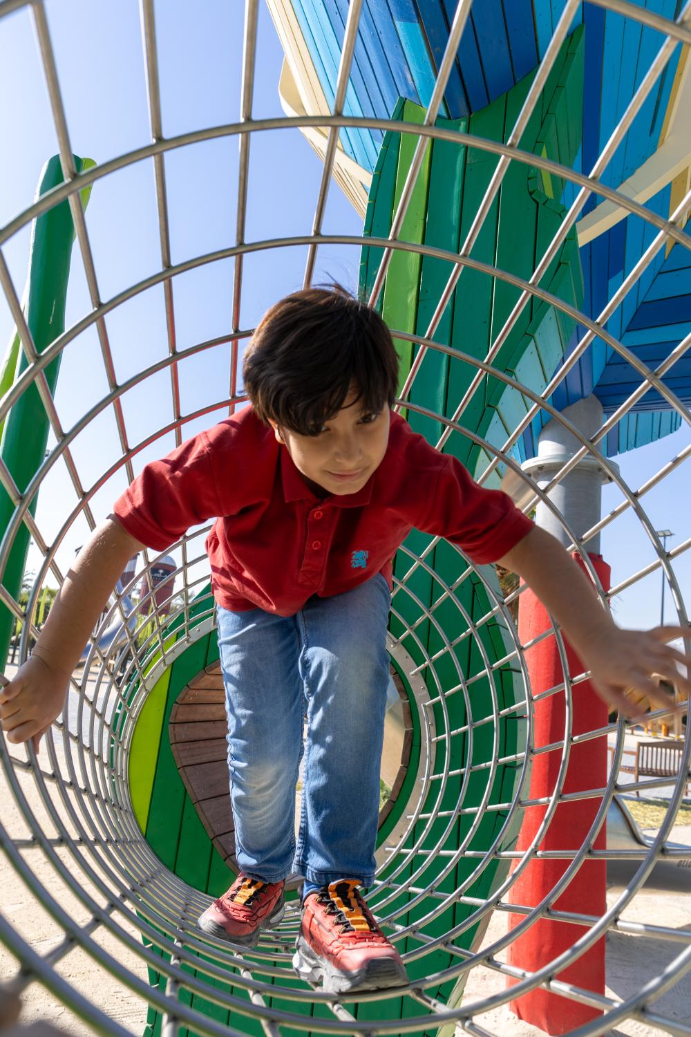 Boy climbing through steel mesh tunnel at playground