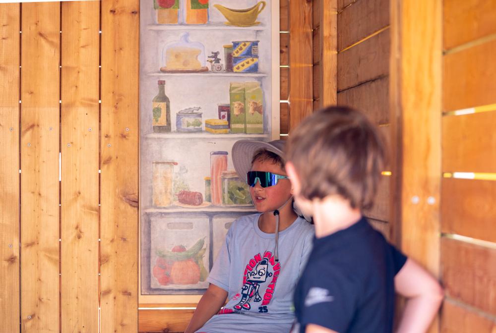 Boys playing inside playground house with painted refrigerator details