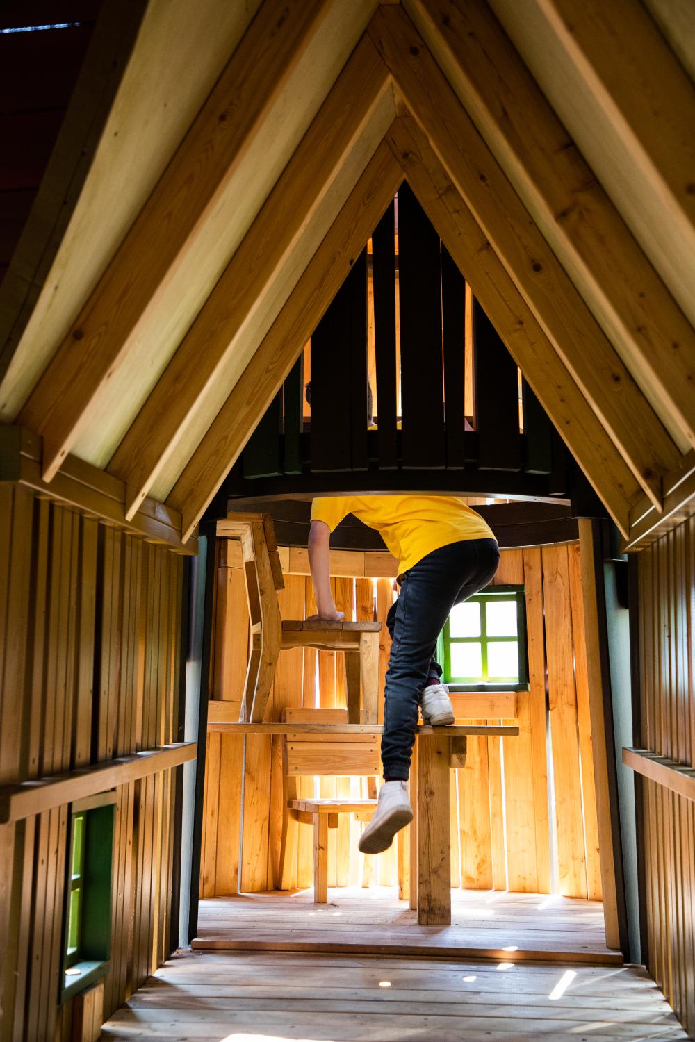 Child climbing up inside of wooden playground structure