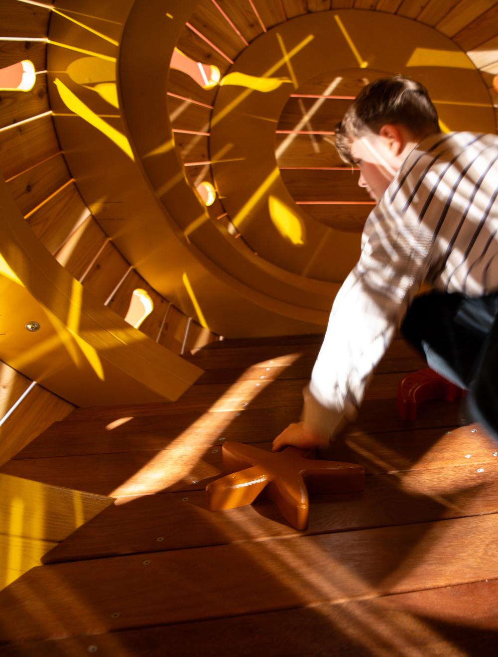 boy climbing inside wooden playground structure