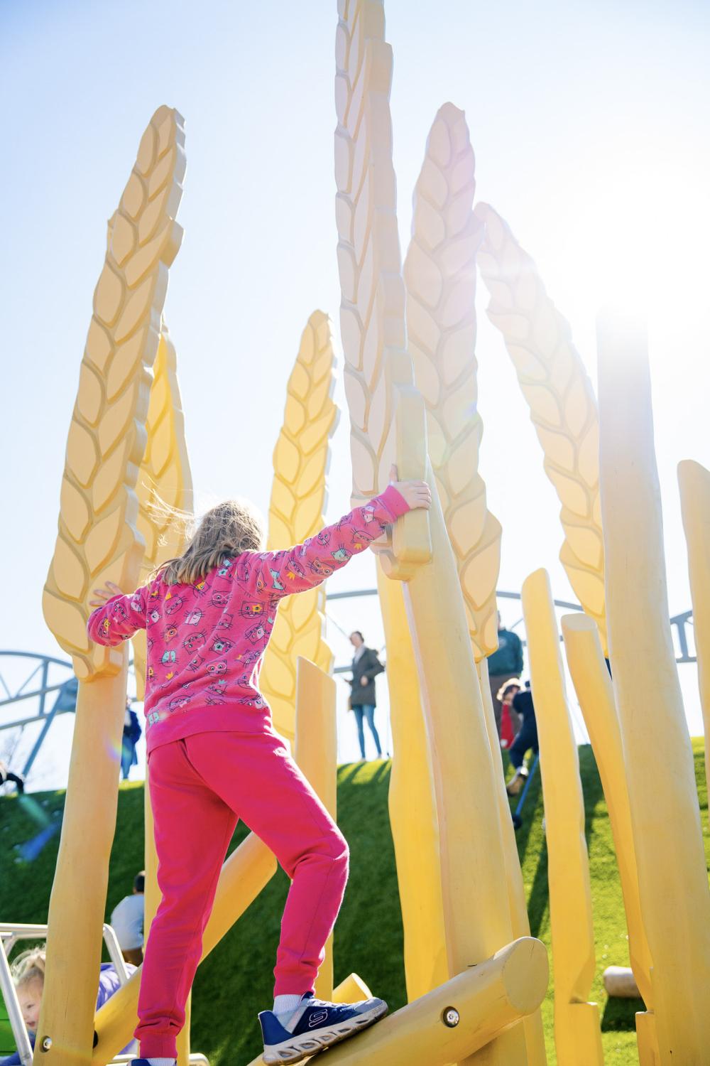 Girl climbing on wooden wheat play features at agriculture-themed playground
