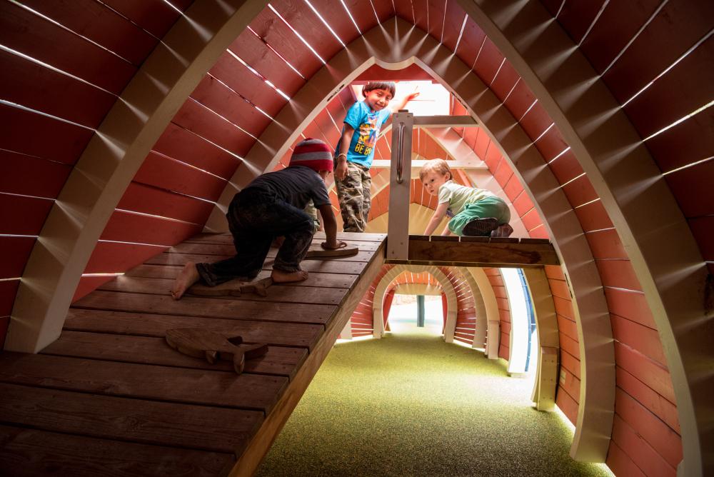 Kids playing inside creative wooden playground structure