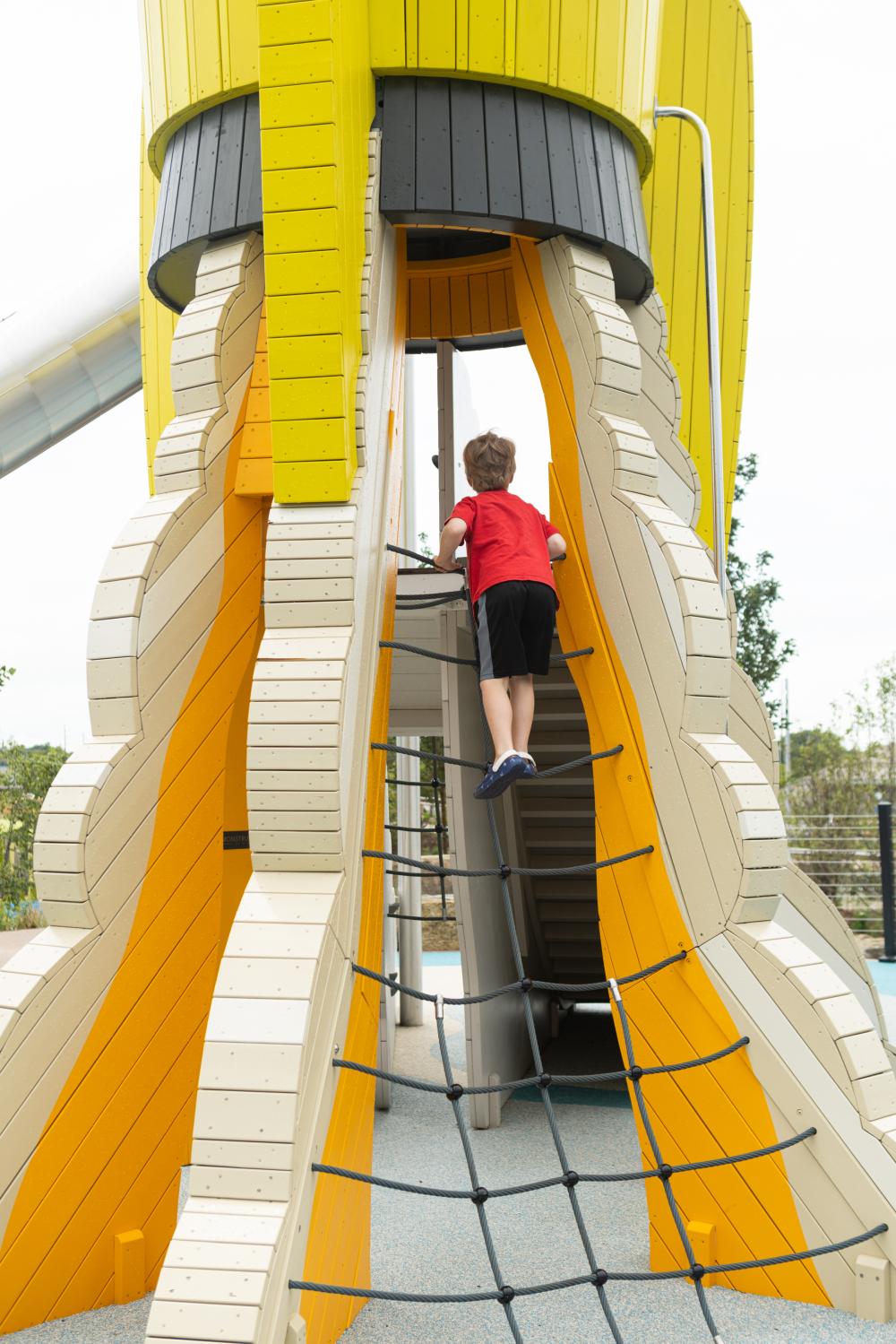 Boy climbing up rope net ladder to wooden rocket at playground