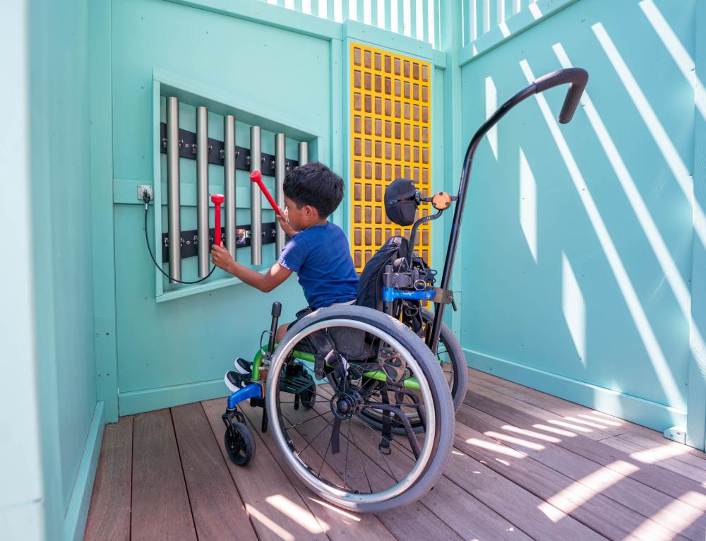 Boy with impaired mobility playing on chimes at playground