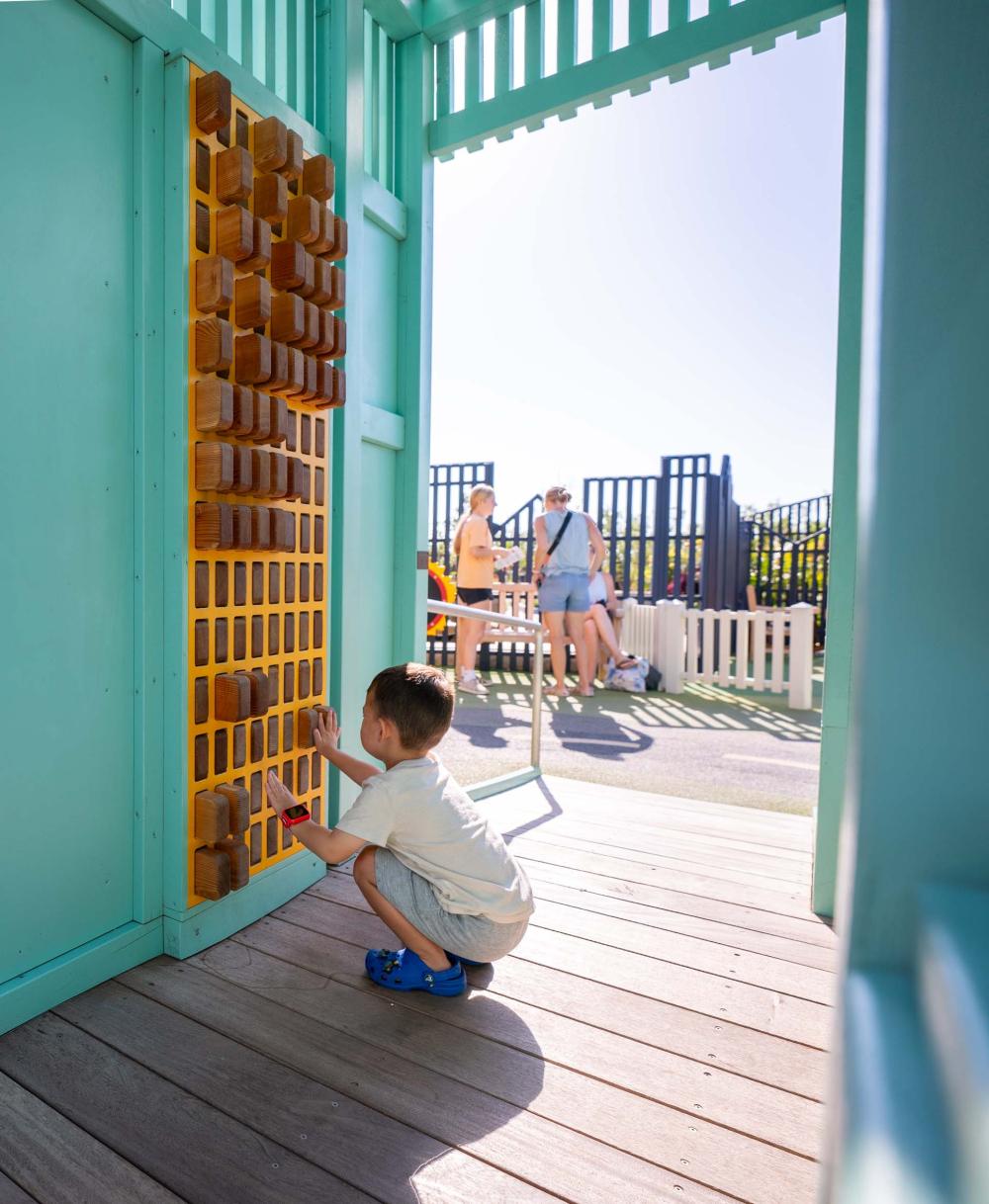Boy playing on pin wall feature at inclusive playground