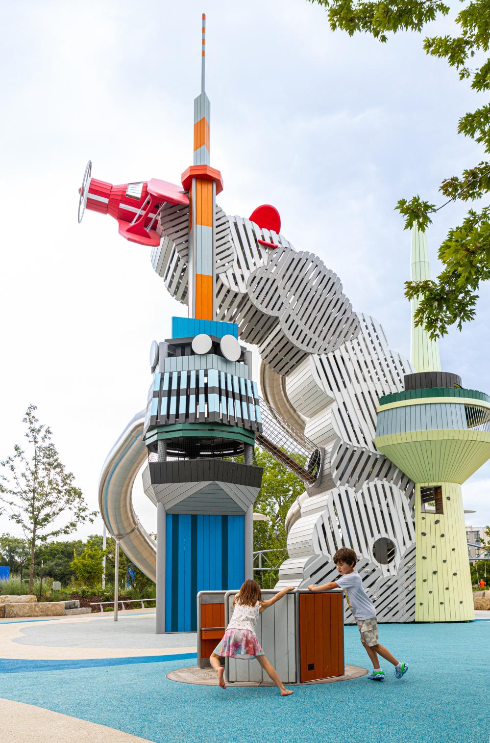 Children playing on carrousel with a huge plane-themed play structure in the background
