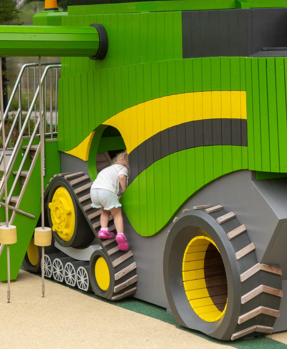 Kid climbing into wheel of wooden playground combine harvester